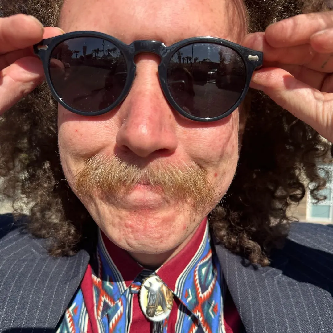 Headshot of Side Hustle Art Show artist, Brillo wearing sunglasses, button-up shirt and blazer