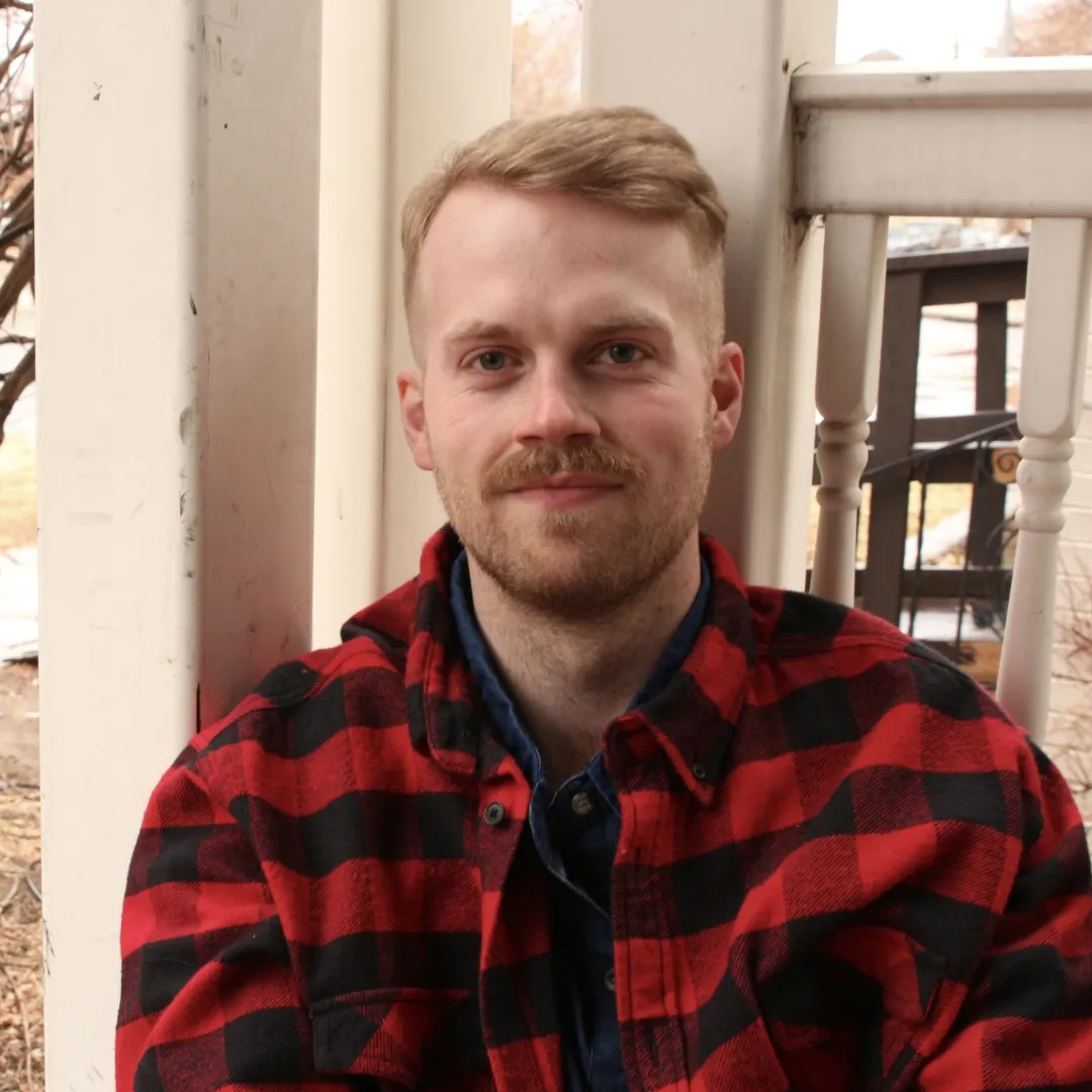 a headshot of Side Hustle Art Show artist Cooper Smith wearing a black and red flannel shirt looking at the camera