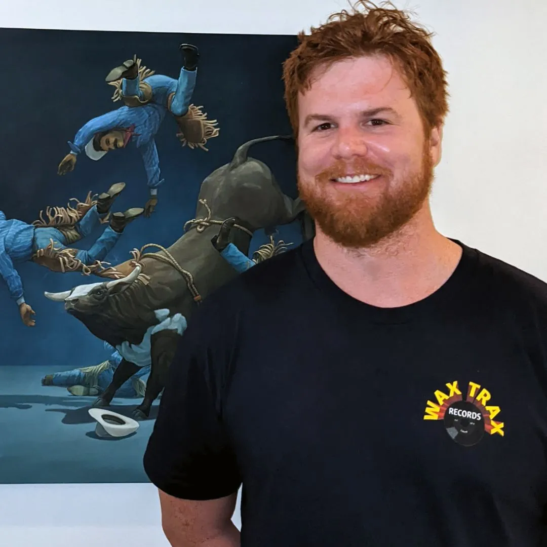 Headshot of Side Hustle Art Show artist, Will Barker wearing a dark navy shirt standing in front of one of his paintings